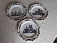 Set of three Gien porcelain plates displayed on table, showing black transferware scenes with floral borders