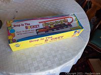 Original sealed game box of Drop In The Bucket, showing colorful packaging on a table.