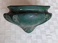 Top view of the green pottery wall pocket showing trapezoidal shape with embossed floral details and green glaze with some wear spots.