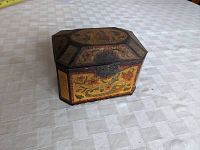 Angled front and side view of the antique English tea tin showing floral painted decoration and hinged lid with clasp.