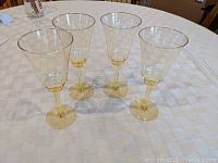 Four yellow tinted Depression glass wine stems/water goblets placed on a white checkered tablecloth, showing their full height and shape.