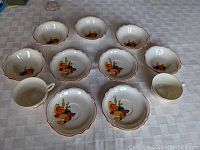 Overview of all 11 pieces including 5 fruit bowls, 2 cups, and 4 saucers with Mexicana decoration on white ceramic with red scalloped rims.