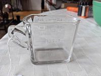 Clear glass measuring cup with measurement markings visible on the side and handle, placed on white textured surface.
