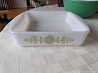 Front and side view of the white square Glasbake baking pan showing the green stylized floral pattern and shape.