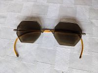 Top-down view of octagonal olive green lenses with thin wire frames, resting flat on a white surface, showing yellow wrapped arms.