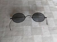 Top down view of antique oval wire frame sunglasses with grey smoke lenses laid on beige patterned surface.