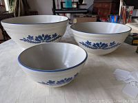 Three nested Pfaltzgraff Yorktowne mixing bowls showing blue floral design on off-white ceramic.