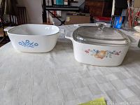 Side view of the two Corning Ware casserole dishes showing the Blue Cornflower and Abundance patterns and glass lid on top of the Abundance dish.