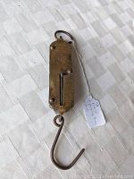 Front view of antique brass hanging scale showing the measuring slider, hook at bottom and suspension ring at top, placed on textured fabric.