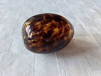 Side view of the mottled amber colored glass darning egg showing its polished surface and size.