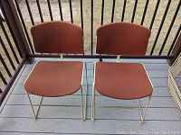 Front view of two Steelcase mid-century stacking chairs with rust-colored upholstery and light metal frames on a porch deck.