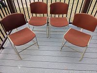 Front view of 4 Steelcase mid-century stacking chairs arranged in two rows on a gray deck, showing orange fabric upholstery and metal sled base frames.