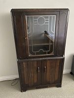 Front view of the antique 1920's Art Deco china cabinet showing the glass door with geometric pattern, wooden lower doors with vertical line detailing, and rounded edges.