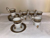 Six white porcelain footed cups with ornate 24K gold plated handles, feet, and decorative band near rim, each paired with matching gold-edged saucers.