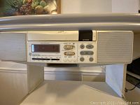 Close-up of the white undermount radio/CD player showing digital display and control buttons, speaker on the right side.