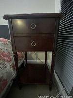 Front and side view of the dark brown wooden end table with two drawers and lower open shelf, showing minor surface scratches.