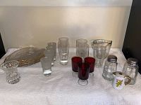 Wide shot showing the entire assortment of glassware including four red shot glasses, four clear glasses, four gold-trimmed glass plates, measuring glass, salt and pepper shakers, crystal toothpick holder, and ceramic egg cup.