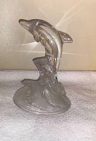 Clear glass dolphin figurine on textured wave base, showing side profile of the figurine and base details.