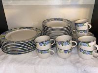 Photo showing stacked dinner plates, salad plates, and a row of teacups with hydrangea pattern.
