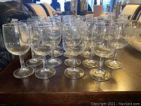 Photo of 19 clear stemmed wine glasses arranged on a dark wooden surface, showing various shapes and sizes.