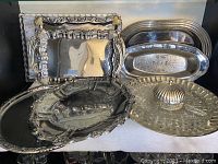 Various silver serving trays, rectangular and oval, with polished finish and decorative details.