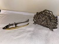 Photo showing a two-tone fish motif nutcracker and a metal rose designed napkin holder on a white cloth surface.