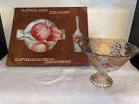 Cake plate with matching server in original packaging alongside decorative colored glass bowl.