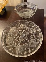 Photo showing both the round serving tray with etched floral design and the clear glass bowl with vertical ribbed sides and two handles.