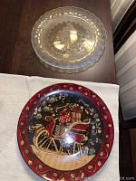 Top-down photo showing two plates on a table, one clear glass plate with scalloped edges and one colored Christmas plate with sleigh design.