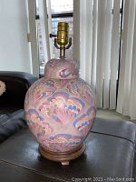 Close-up of a single ceramic lamp showing rounded body with marbled pastel colors and brass lamp fitting on wooden base.
