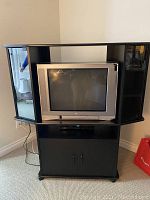 Front view of black TV unit with glass doors and CRT TV inside