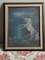 Framed print of a unicorn under a moonlit sky, in a wooden frame with a gold-toned inner border.
