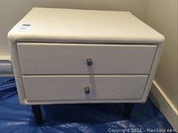 Front view of square side table showing two drawers and metal knobs, covered in light-colored faux leather fabric.