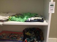 Photo showing two shelves with folded fabric items including scarves and tops in various colors, some with tags