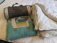 Rolled Bamboo Memory Foam pillow in packaging alongside folded white duvet and colorful llama pillow on bed
