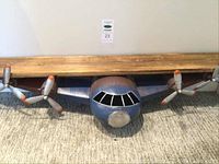 Full frontal view of plane shaped shelf with wooden shelf on top and metal airplane body with twin propellers and cockpit window cutouts.
