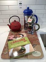 Overview of the lot showing two French presses, a red iron cast teapot, cutting board, and cookbook