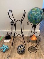 Photo showing all six items: mosaic gazing ball on stand, smaller marbled glass ball, solar shell light, plasma ball lamp, decorative blue starfish, and empty black metal stand.