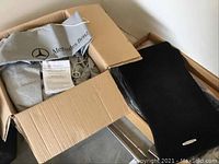 Box containing Mercedes-Benz storage bag and folded car cover, plus black floor mat
