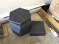 Stack of 16 black plastic textured hexagonal pavers with 4 black square pavers beside it.