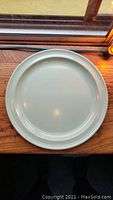 Single green dinner plate with raised rim centered on wooden surface near a window showing color and shape.