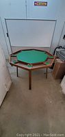 Wide view of the octagonal foldable poker table showing green felt center, wooden frame, and three supporting legs.