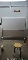 Full view of the large whiteboard on wheels standing against a wall with a stool in front.