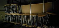 Multiple stools stacked on metal shelving, showing oak seats and grey steel bases.