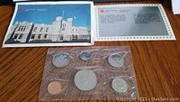 Photo of the sealed 1987 uncirculated Canadian coin set in plastic packaging alongside the informational brochure featuring the Royal Canadian Mint building.