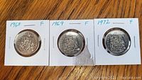 Obverse side of 1968, 1969, and 1972 Canadian fifty cent coins showing the Canadian coat of arms.