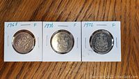 Obverse side of 1968, 1970, and 1972 Canadian fifty cent coins showing the Canadian coat of arms, each secured in individual coin holders.