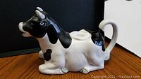 Side view of cow-shaped ceramic teapot showing black and white Holstein pattern with spout at mouth and handle at rear