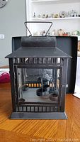 Front view of black metal lantern style tealight holder with glass panes and four tealight holders inside