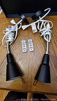Two Ikea black LED lamps with flexible gooseneck arms and attached power cords placed on a wooden surface alongside two small metal mounting brackets